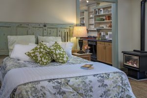 queen bed with green & white print bedspread, table lamp, bookshelves on right