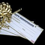 stack of three gold-edged white gift certificates decorated with elaborate gold ribbon bow, black background