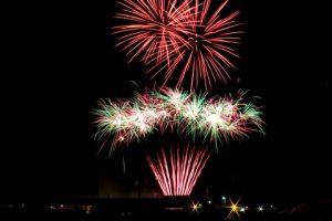 fireworks in night sky - two large red starbursts above vertical traces to white, green, red smaller starbursts