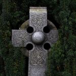 Closeup of gray Celtic cross tombstone with greenery background by Adrian Moran on UnSplash