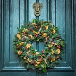 Holiday wreath with red and yellow fruit decorations on blue-green paneled door with by Jez Timms on UnSplash