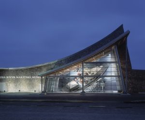 Lighted glass and gray stone triangular facade of Columbia River Maritime Museum at night