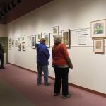 white art gallery wall with paintings, four people wearing red or blue jackets looking at art