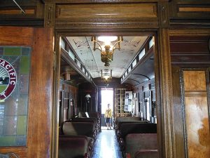 view through door to Columbia Pacific Heritage Museum railroad coach with seats, hanging lights, boy standing at end of car