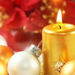 one white and one gold Christmas tree balls leaning against lighted gold cylinder candle, red petals in background