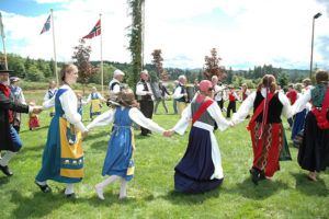 ring dancers in Scandinavian costumes on green lawn at Astoria Oregon Midsummer Festival