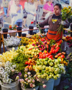 woman in red apron holding bunch of flowers standing behind buckets of tulips and other flowers at Astoria Sunday Market