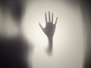 gray silhouette of hand held up with fingers spread surrounded by whitish fog