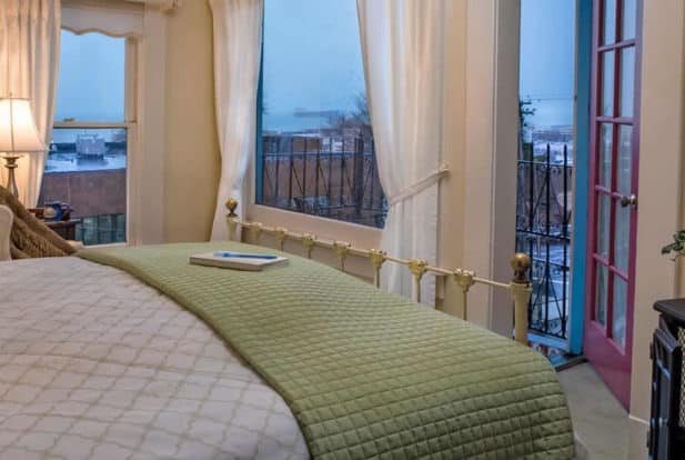 Painted brass bed made up in white and green faces an open door to a wrought iron balcony.