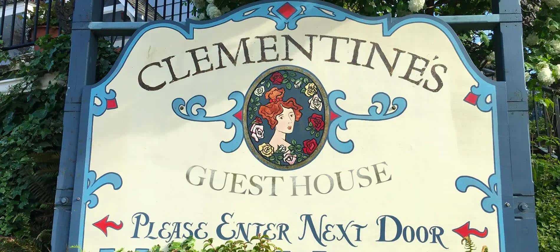 Large wooden sign with a blonde Victorian woman that says Clementine's Guest House - Please Enter Next Door.