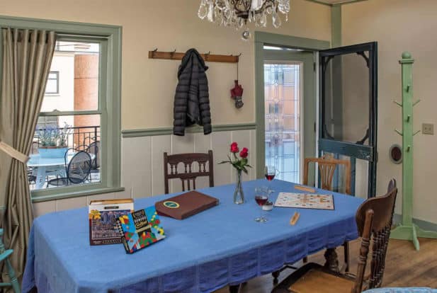 Large table with a blue cloth set up with board games in a room with wooden floors and a door out to the porch.