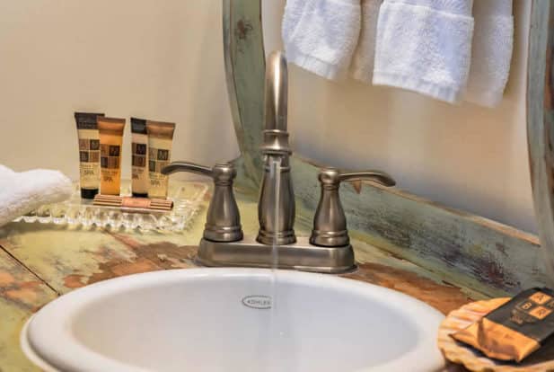 A white sink inset into a shabby-chic wooden vanity with a polished silver faucet.