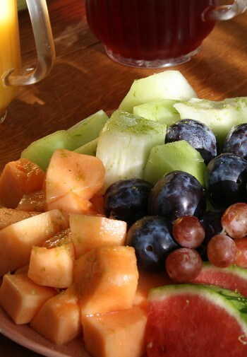 Plate packed with fresh fruit - watermelon, canteloupe, honeydew, and grapes on a table with juice.