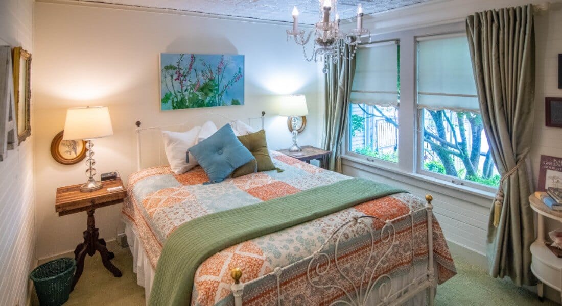 Bright bedroom with a white wrought iron bed covered in an orange paisley comforter